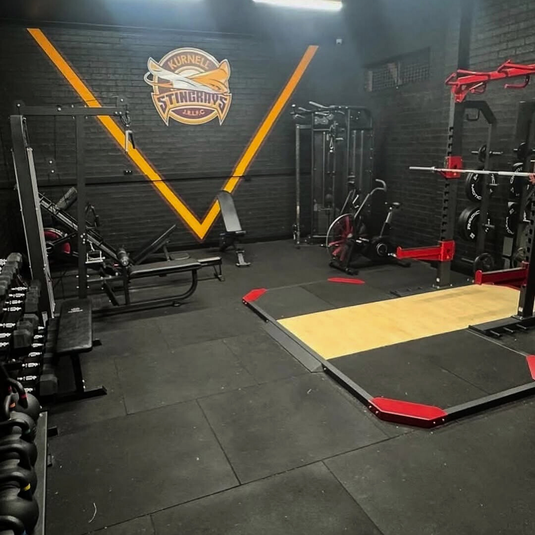 A gym interior featuring weights, exercise equipment, and a logo on the wall.
