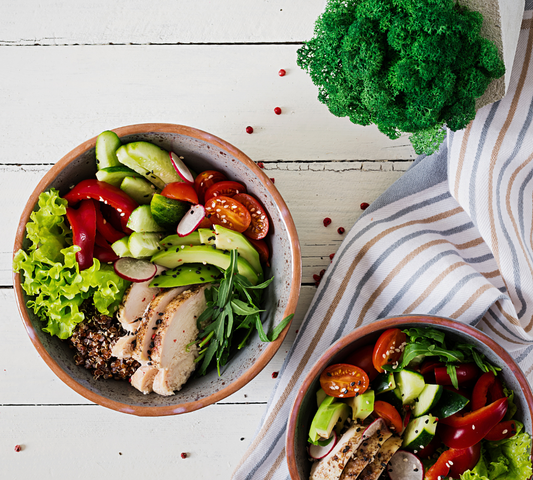 Two bowls of fresh salad with vegetables and grilled chicken on a wooden table.
