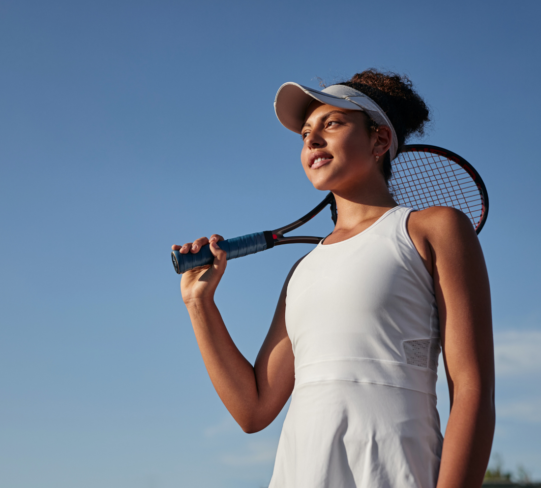 Young woman holding a tennis racket against a clear blue sky.