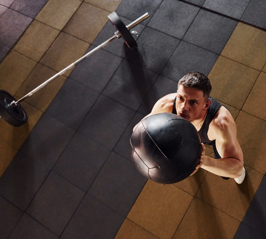 Man lifting a medicine ball in a gym setting.