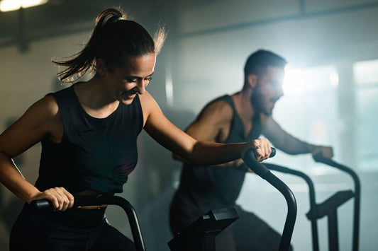 Two individuals exercising on elliptical machines in a gym setting.